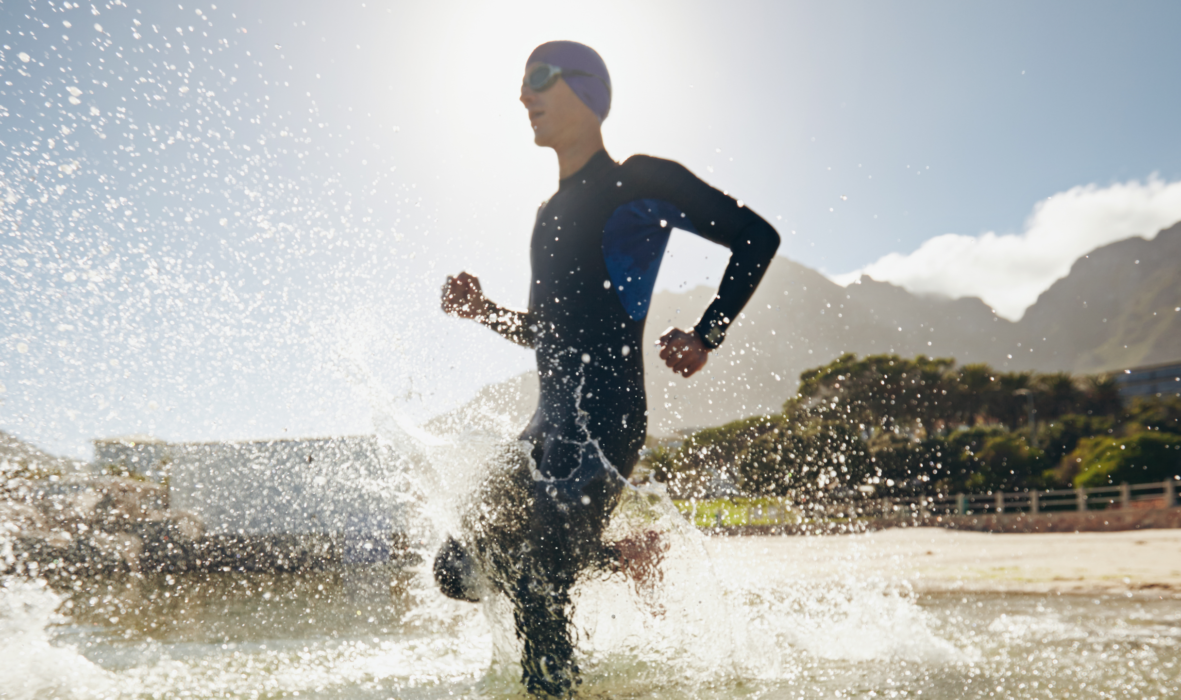 Photo of triathlete running into the water from the shoreline, while wearing a wetsuit, swim cap an goggles.